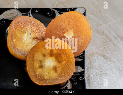 On the table on a glass dish is the sliced persimmon. Stock Photo