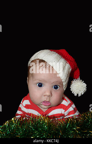 Newborn funny Santa baby with dumbfounded face isolated on black background.  Can be used for design of banners, flyers, calendars, invitations  as cl Stock Photo