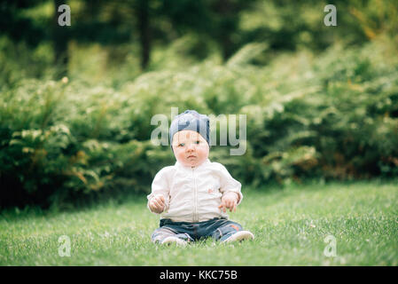 Portrait of cute baby with big blue eyes dressed in white shirt, on natural green background with grass, bushes and soap bubbles around. Stock Photo