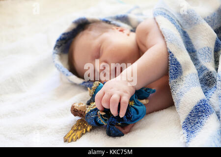 Christmas baby. Portrait of cute newborn baby sleeping in blue blanket with figure of angel in hands on white background. Stock Photo