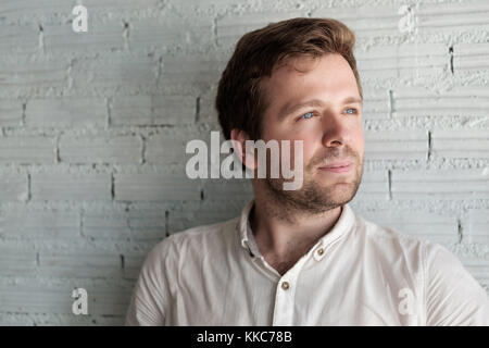 Caucasian man in white shirt standing near wall and smile a little. He is content and confident. Stock Photo