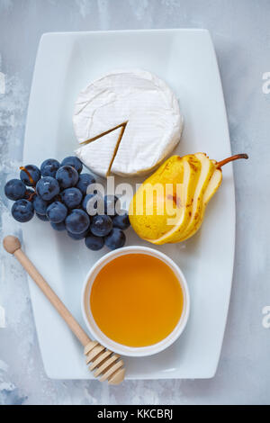 Cheese brie (camembert) with honey and fruits on a white plate. Light background, top view. Stock Photo