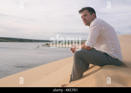 Lonely Man sitting on sand beach and watching far a way views alone. Stock Photo