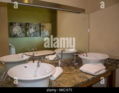 Modern bathroom with two elegant retro white ceramic wash basins against mirror on marble table top stand with Victorian bath reflected in mirro Stock Photo
