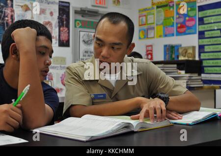 Personnel Specialist Seaman Fung Chan, assigned to submarine tender USS Emory S Land AS 39, explains math concepts and formulas to a student from Jose Rios Middle School as part of the Saturday Scholars tutoring program, Piti, Guam. Image courtesy Information Systems Technician 2nd Class Alexavier Allen/US Navy. 2012. Stock Photo