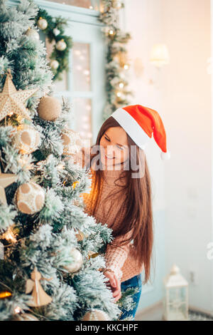 Happy young woman holding Christmas ball in front of Christmas tree Stock Photo