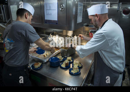 BANGOR, Wash. (Nov. 28, 2017) Electrician’s Mate (Nuclear) 3rd Class Stephen Ingui, left, assigned to the Gold crew of the Ohio-class ballistic missile submarine USS Louisiana (SSBN 743), from Warwick, New York, prepares bread pudding with Christopher Lusk, executive chef from the New Orleans restaurant The Caribbean Room. Sponsored by the New Orleans Navy League, Lusk traveled from New Orleans, Louisiana, with David Whitmore Jr., the chef de cuisine for Borgne Restaurant, to donate ingredients and cook Louisiana-inspired cuisine for the 300-crew members on board the submarine. (U.S. Navy phot Stock Photo