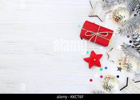 silver christmas tree branch decorated with toys and glowing garlands, confetti, gingerbread cookies and red gift box on white wooden background with  Stock Photo