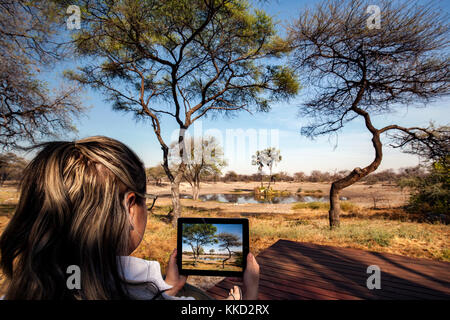 Young woman taking picture with tablet at Onguma Tented Camp, Onguma Game Reserve, Namibia, Africa Stock Photo