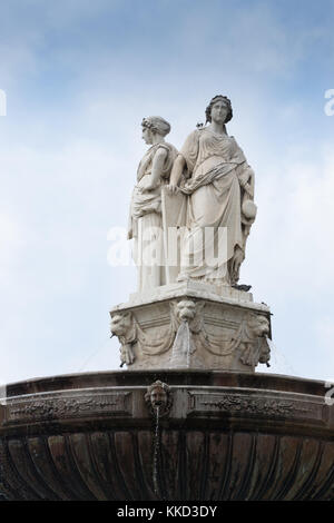 Close up of a fountain topped with two carved statues of women in long gowns standing on a pedestal. Gargoyle fountains are at the base of the statue. Stock Photo