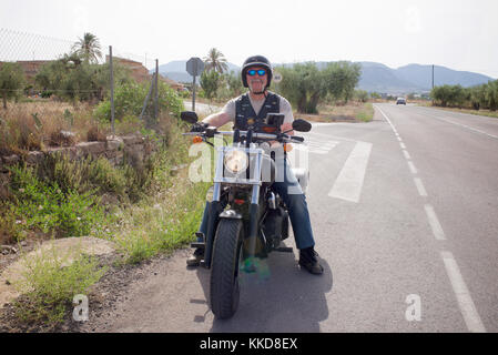 Man sitting on a Harley Davidson motorcycle by the roadside Stock Photo