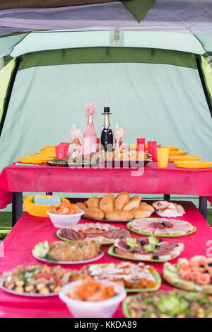 Wedding outdoor  table with various dishes on it with two bottles of champagne beautifully decorated like bride and groom in head of it. Stock Photo