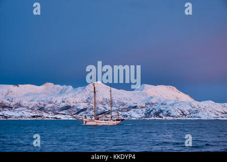 sunrise over fjord with snow covered mountains and winter landscape and sailship near Tromso, Troms, northern Norway, Europe Stock Photo