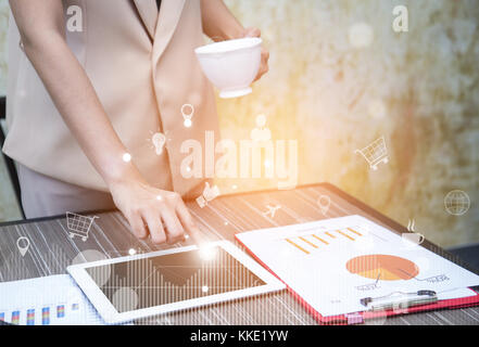 Analysis of large data and business concepts (BI) business women holding a cup of coffee and finger typing tablet with virtual icons on the background Stock Photo