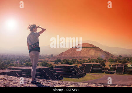 Young woman standing on top of pyramid and overlooking Teotihuacan in orange sunset light Stock Photo