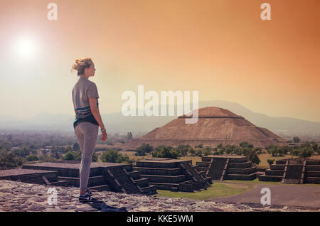 Young woman standing on top of pyramid and overlooking Teotihuacan in orange sunset light Stock Photo