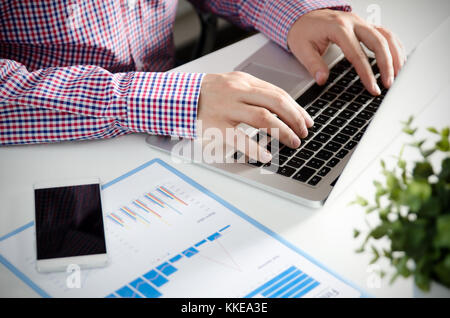 Man using mobile phone while working on laptop. Working with financial statement document Stock Photo