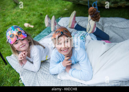 Big Wild Sleepout event pix . Images of young kids/ children and parents out in their back garden from around mid-afternoon until night-time, enjoying activities, such as  making a den, looking at bugs, putting out dog food for hedgehogs, toasting marshmallows around a fire pit, moth trapping, looking for nocturnal wildlife. Stock Photo