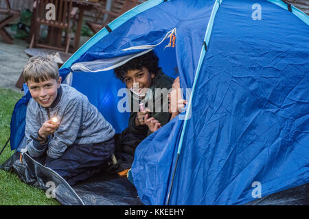 Big Wild Sleepout event pix . Images of young kids/ children and parents out in their back garden from around mid-afternoon until night-time, enjoying activities, such as  making a den, looking at bugs, putting out dog food for hedgehogs, toasting marshmallows around a fire pit, moth trapping, looking for nocturnal wildlife. Stock Photo