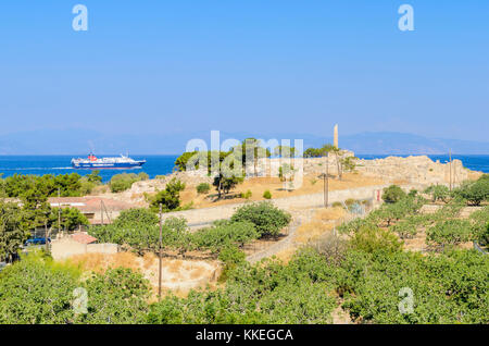 A ferry travels through the Saronic Gulf past the lone column of the Temple of Apolloon the ancient Hill of Koloni, Aegina, Greece Stock Photo