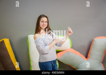 Confident young woman giving the thumbs up against a gray background. Stock Photo