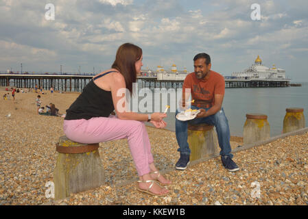 A couple eating chips on Eastbourne beach, East Sussex, England, UK Stock Photo