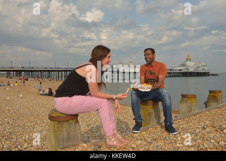 A couple eating chips on Eastbourne beach, East Sussex, England, UK Stock Photo