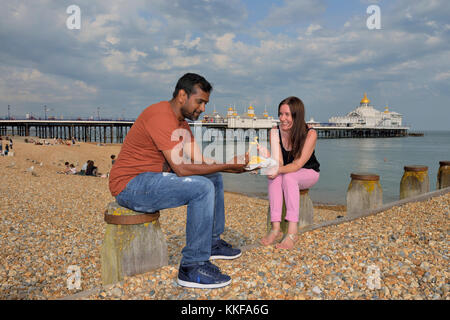 A couple eating chips on Eastbourne beach, East Sussex, England, UK Stock Photo
