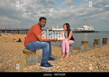 A couple eating chips on Eastbourne beach, East Sussex, England, UK Stock Photo