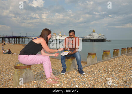 A couple eating chips on Eastbourne beach, East Sussex, England, UK Stock Photo