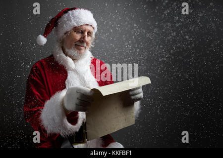 Happy Santa Claus holding vintage paper on dark background. Merry Christmas and New Year's Eve concept. Stock Photo