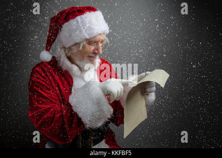 Happy Santa Claus holding vintage paper on dark background. Merry Christmas and New Year's Eve concept. Stock Photo