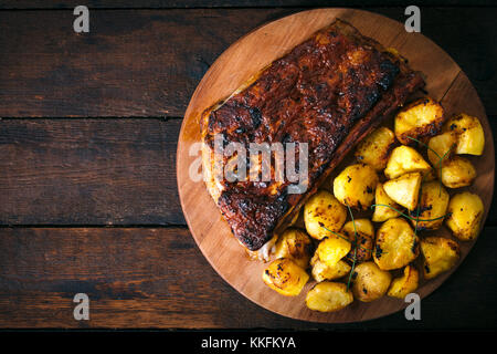 Baked potatoes and beef ribs in bbq sauce from above on wooden background.Blan space on the left side Stock Photo