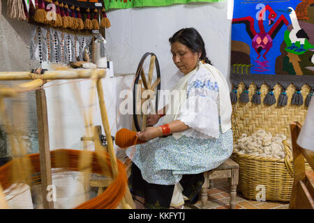 Ecuador Culture - an ecuadorian mature woman using a traditional spinning wheel spinning yarn to make textiles, Otavalo, Ecuador, South America Stock Photo