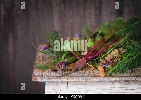 Assortment of fresh herbs mint, oregano, thym, blooming sage and young vegetables beetroot and carrot over old wooden stool as background. Natural day Stock Photo