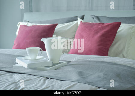 Ceramic tea set and books setting on bed with red velvet pillows Stock Photo
