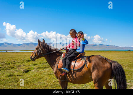 SONG KUL, KYRGYZSTAN - AUGUST 11: Two kids riding and greeting from a horse by Song Kul lake. August 2016 Stock Photo