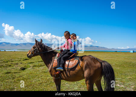 SONG KUL, KYRGYZSTAN - AUGUST 11: Two kids riding and greeting from a horse by Song Kul lake. August 2016 Stock Photo
