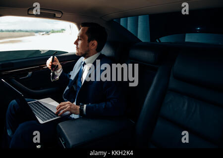 Serious businessman in a car with laptop Stock Photo