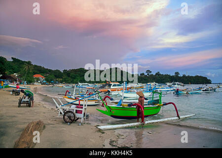Balinese fishermen with traditional outrigger fishing boats in the bay of Padang Bai / Padangbai / Padang Bay at sunset on the island Bali, Indonesia Stock Photo