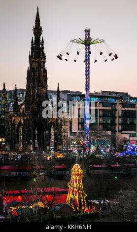 Edinburgh, Scotland, United Kingdom, 30th November 2017.  Edinburgh Christmas celebrations Christmas Market and fairground rides, with a star flyer in action next to Scott.Monument in Princes Street Gardens and a Hester Skelter in the foreground.  The city centre is lit up with wonderful colourful lights at sunset on a Winter evening