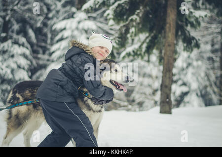 little girl with beautiful big dog in the forest in winter time Stock Photo