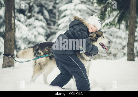 little lovely girl hugging a beautiful big dog in the forest in winter time Stock Photo