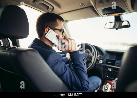 Man in the car reading and phoning Stock Photo