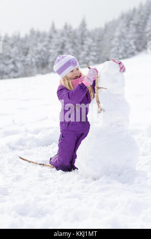 little girl in the forest building the snowman Stock Photo