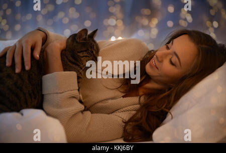 happy young woman with cat lying in bed at home Stock Photo