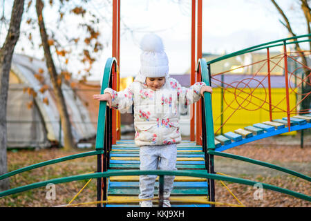 Little girl is playing on the playground in the park. The child goes on the steps of the playground Stock Photo