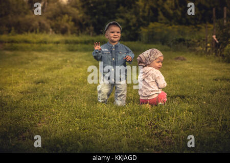 couple of cute children boy and girl playing together on grass at sunset in rural field in countryside symbolizing carefree and happy childhood Stock Photo