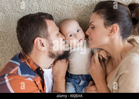 happy family lying on floor and kissing their baby Stock Photo