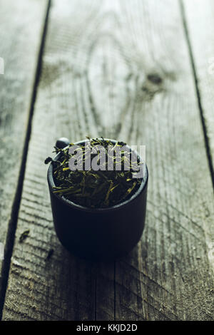 Dry organic green tea leafs in a black cup on a wooden background Stock Photo